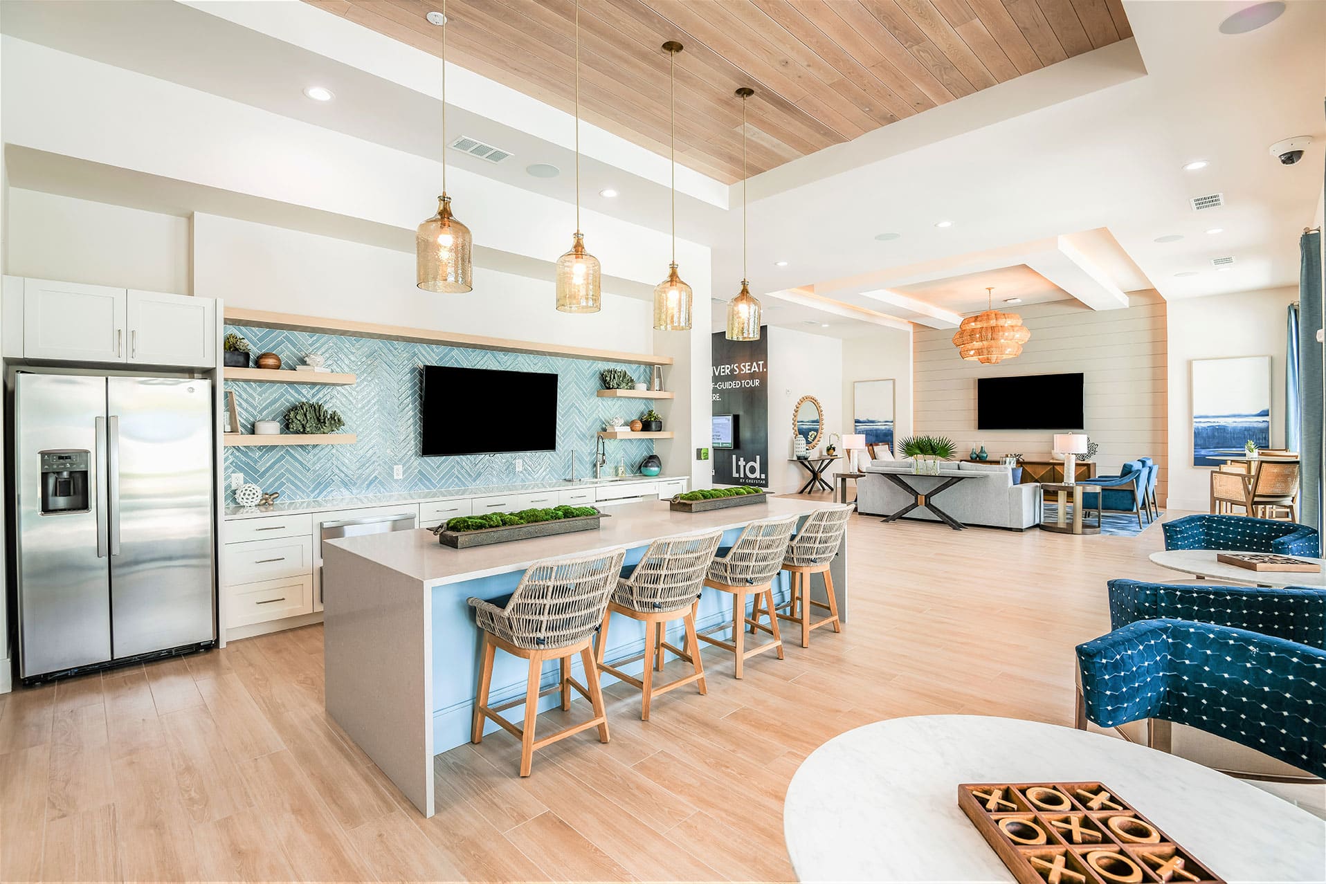 Open-plan kitchenette with blue herringbone backsplash, bar seating, pendant lights, and an adjoining communal lounge area.